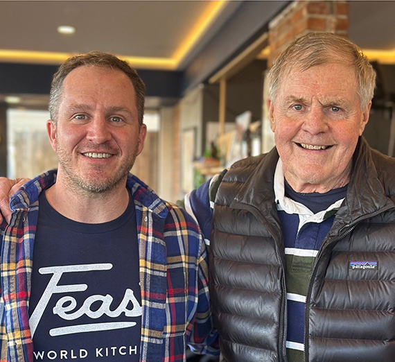 two people hoist a large tree into a hole next to a trail